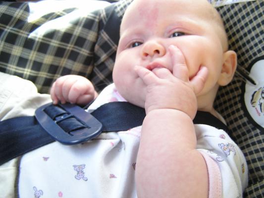 Sarah sucks her ring finger in her carseat.