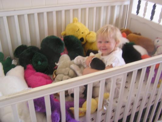 Sarah is playing in her crib with stuffed toys.