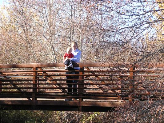 Noah and Katie on a bridge by the woods.