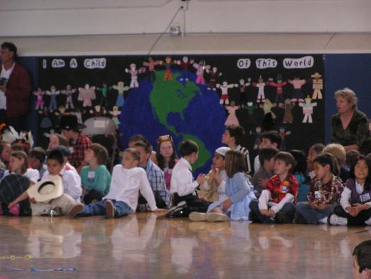 Several children sit in front of a banner. The banner shows the dolls children decorated to show their national heritage.