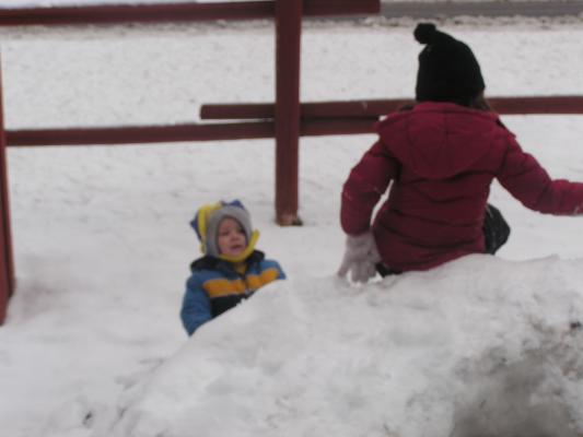 Noah watches Andrea slide down the snowfort.