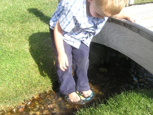 Npah stands on a stepping stone by a little creek.