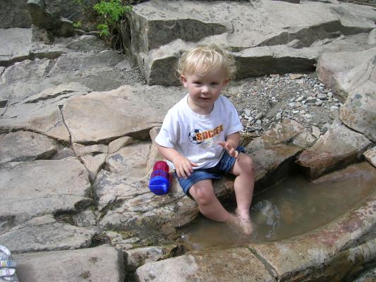 Noah dangles his feet in the puddle of water.