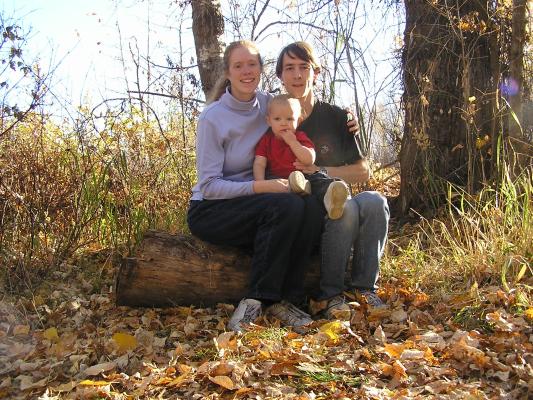 Katie, Noah and David sit on a log in the woods.