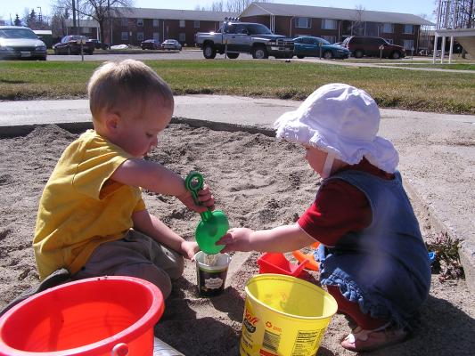 Noah and Sarah fill a yogert container with sand.