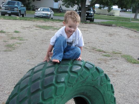 Noah plays on a green tire. 