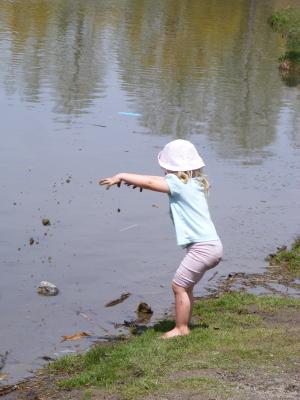 Sarah throws sand in the pond by the mall.