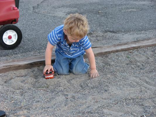 Noah plays with a car in the sand at the park.