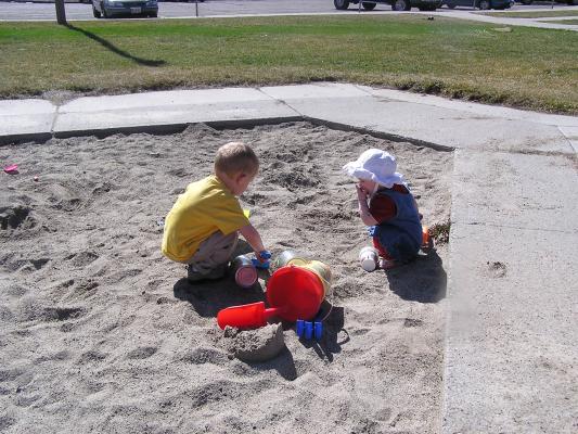 Noah and Sarah play in the sand. Sarah eats it.